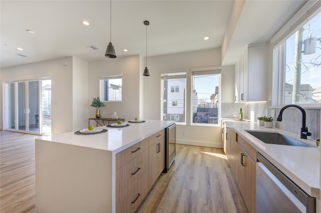 kitchen with modern cabinets, a center island, light brown cabinetry, stainless steel dishwasher, and a sink