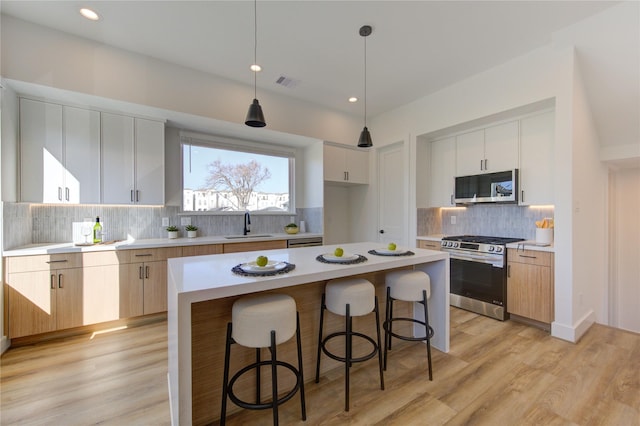 kitchen featuring stainless steel appliances, light countertops, a sink, light wood-type flooring, and a kitchen breakfast bar