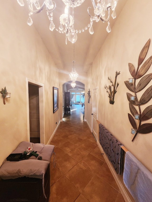 hallway with baseboards, a high ceiling, arched walkways, and a chandelier