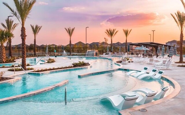 pool at dusk with a jacuzzi, a patio, a community pool, and fence