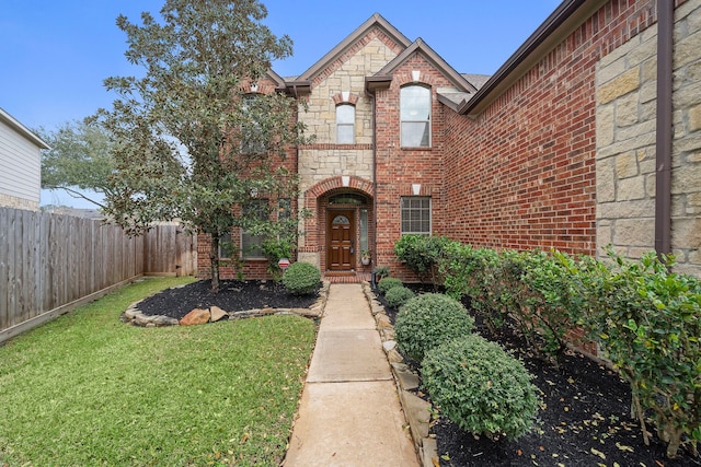 view of front of property featuring a front yard, stone siding, brick siding, and fence