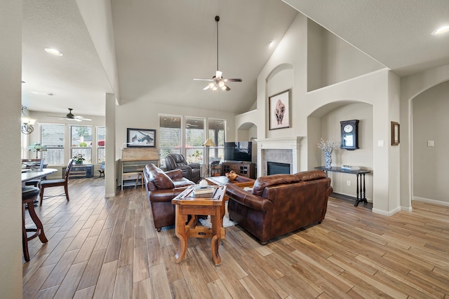 living room with light wood finished floors, ceiling fan, high vaulted ceiling, and a tile fireplace