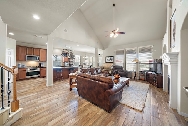 living room featuring a fireplace, light wood-style floors, ceiling fan, high vaulted ceiling, and stairs