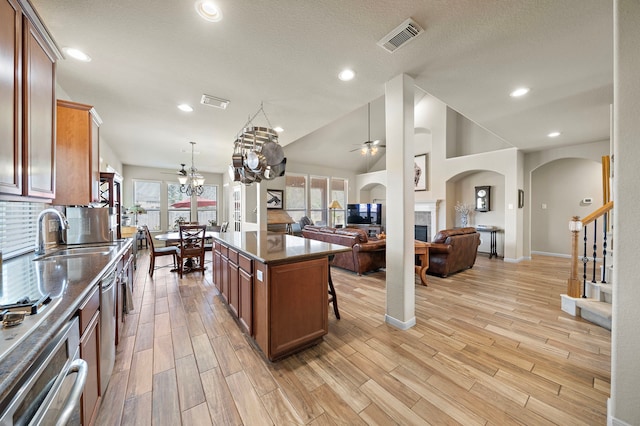 kitchen with visible vents, a tiled fireplace, open floor plan, a sink, and ceiling fan with notable chandelier