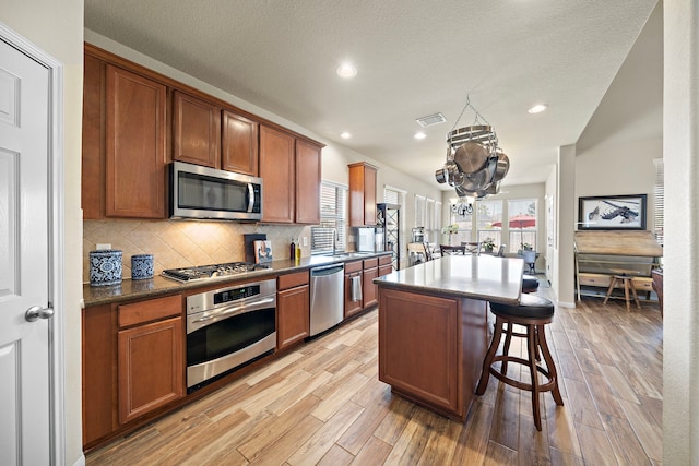 kitchen featuring visible vents, decorative backsplash, a breakfast bar, stainless steel appliances, and light wood-type flooring