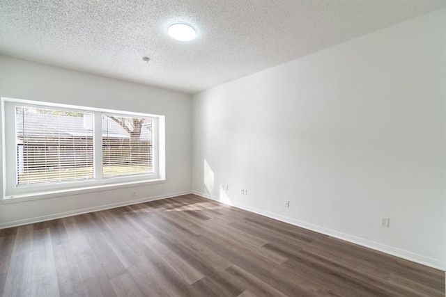 spare room featuring a textured ceiling, dark wood-type flooring, and baseboards