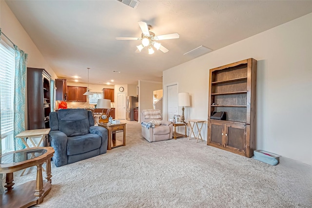 living area with light carpet, visible vents, and a ceiling fan