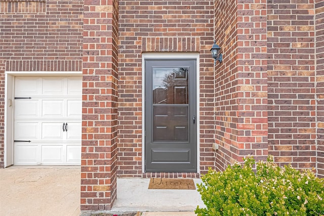 entrance to property featuring a garage and brick siding