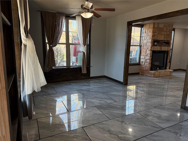 empty room featuring a ceiling fan, marble finish floor, a fireplace, and baseboards