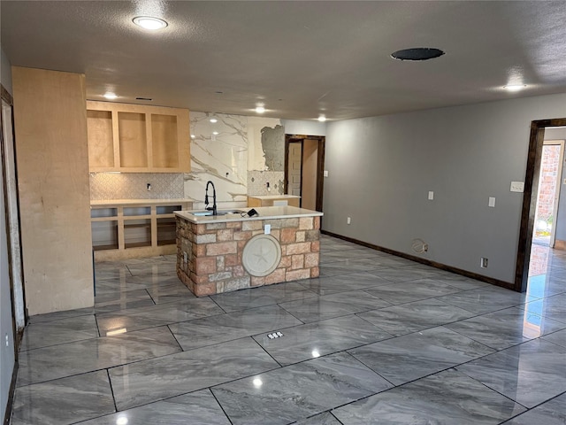 kitchen featuring marble finish floor, a center island with sink, light countertops, backsplash, and a sink