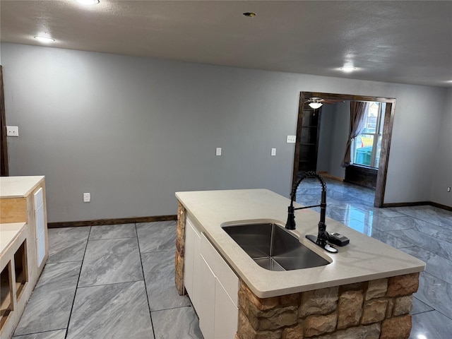 kitchen featuring light countertops, white cabinetry, a sink, and a center island with sink