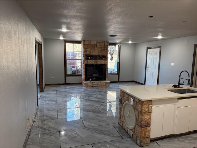 kitchen with a textured ceiling, a stone fireplace, a sink, white cabinets, and marble finish floor