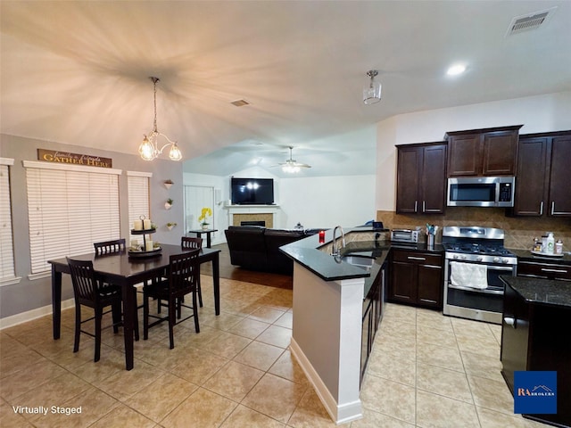 kitchen with a peninsula, a fireplace, a sink, stainless steel appliances, and dark countertops