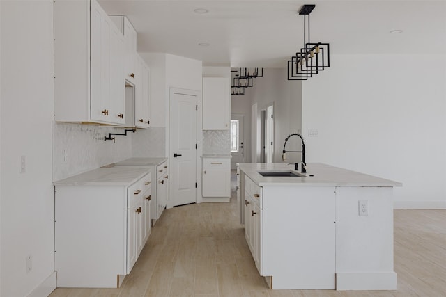 kitchen featuring white cabinets, an island with sink, light wood-style flooring, a sink, and backsplash