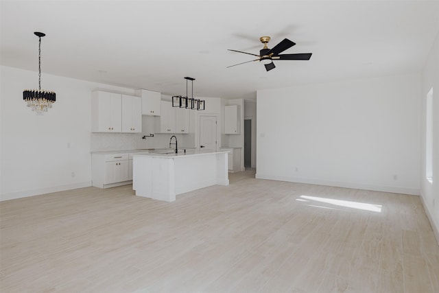 kitchen featuring light wood finished floors, a center island with sink, decorative backsplash, open floor plan, and ceiling fan with notable chandelier