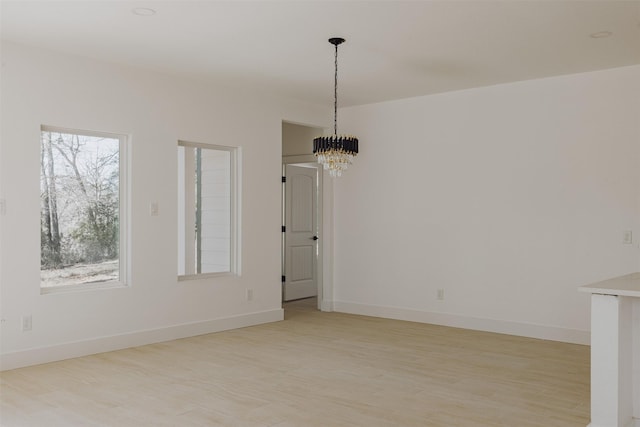 unfurnished dining area with light wood finished floors, an inviting chandelier, and baseboards