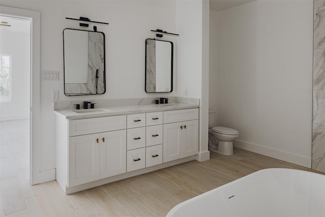 full bathroom with double vanity, a soaking tub, toilet, a sink, and wood finished floors