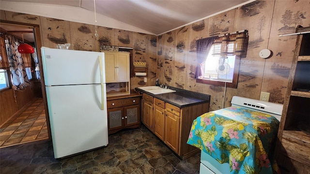 kitchen featuring dark countertops, brown cabinetry, freestanding refrigerator, vaulted ceiling, and a sink