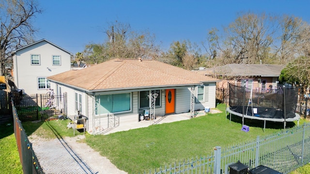 rear view of property with a shingled roof, a patio, a fenced backyard, a trampoline, and a yard