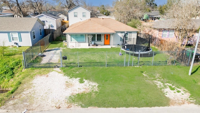 exterior space featuring a fenced backyard, driveway, a residential view, a front lawn, and a trampoline