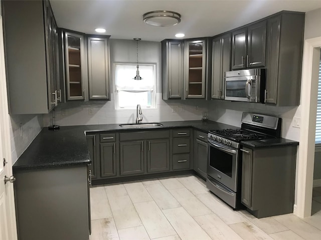 kitchen with appliances with stainless steel finishes, glass insert cabinets, a sink, and decorative backsplash