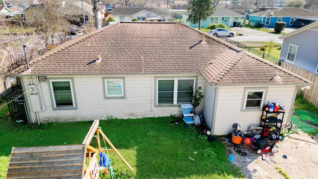 rear view of property featuring a shingled roof, a residential view, fence, and a yard