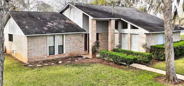 exterior space with roof with shingles, brick siding, and a front lawn