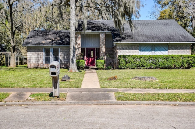 view of front of home with a front lawn, a shingled roof, and brick siding