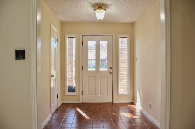 foyer entrance featuring dark tile patterned floors, baseboards, and a textured ceiling