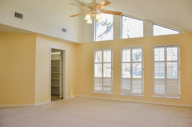 carpeted empty room with a ceiling fan, visible vents, high vaulted ceiling, and a textured ceiling