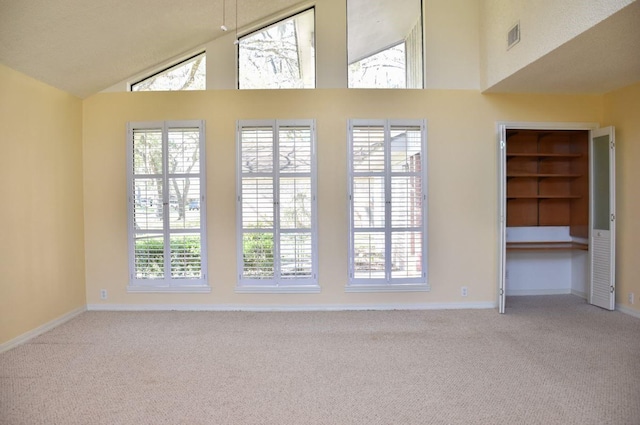 carpeted empty room with high vaulted ceiling and visible vents