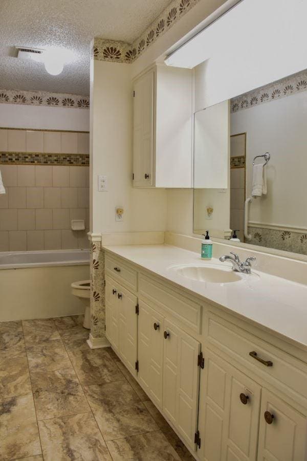 full bath with visible vents, toilet, a textured ceiling, vanity, and washtub / shower combination