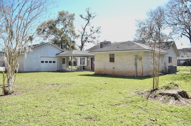 back of property featuring an attached garage, cooling unit, brick siding, a lawn, and a chimney