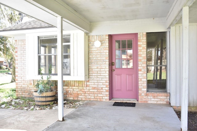 view of exterior entry featuring brick siding and a shingled roof