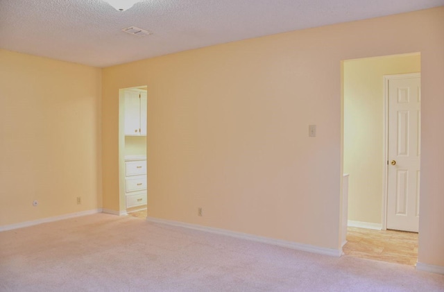 empty room with visible vents, light carpet, a textured ceiling, and baseboards