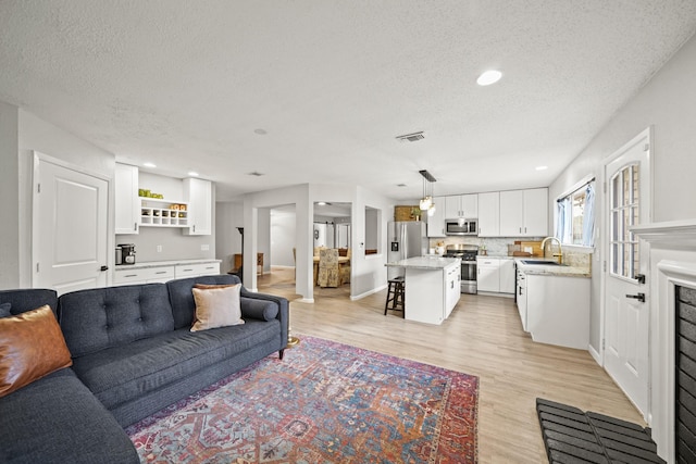 living room with a textured ceiling, recessed lighting, visible vents, and light wood-style floors