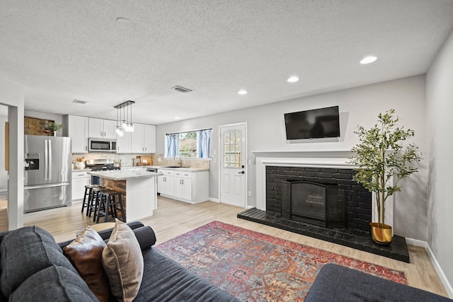 living area with light wood-type flooring, visible vents, a fireplace, and baseboards