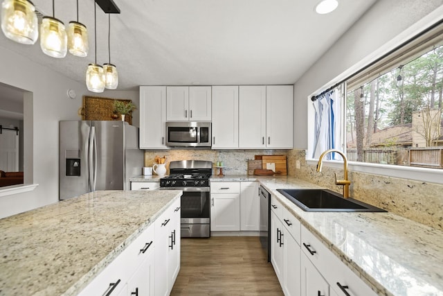 kitchen featuring white cabinets, decorative backsplash, light stone counters, stainless steel appliances, and a sink