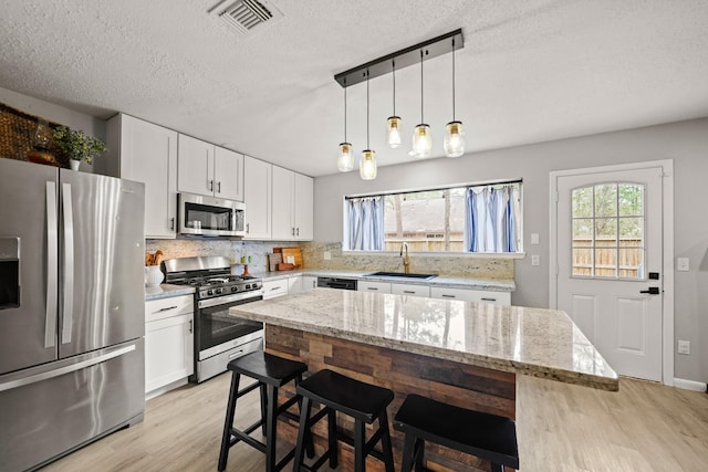 kitchen featuring a sink, visible vents, appliances with stainless steel finishes, light wood finished floors, and tasteful backsplash