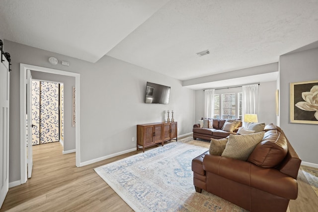 living area featuring light wood finished floors, a barn door, visible vents, and baseboards