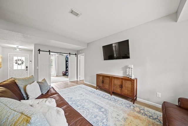 living area with wood finished floors, visible vents, baseboards, and a barn door