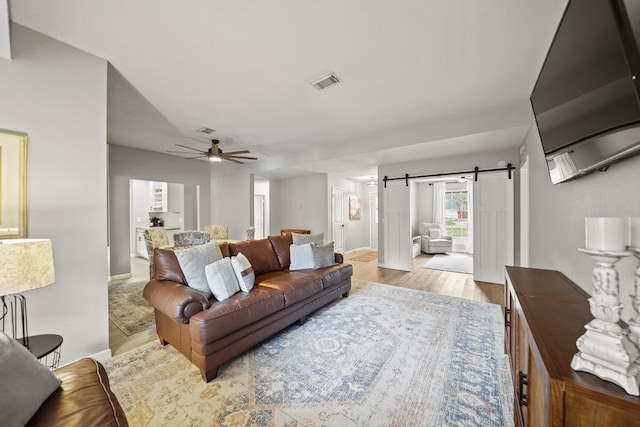 living room with a barn door, visible vents, baseboards, ceiling fan, and light wood-style floors