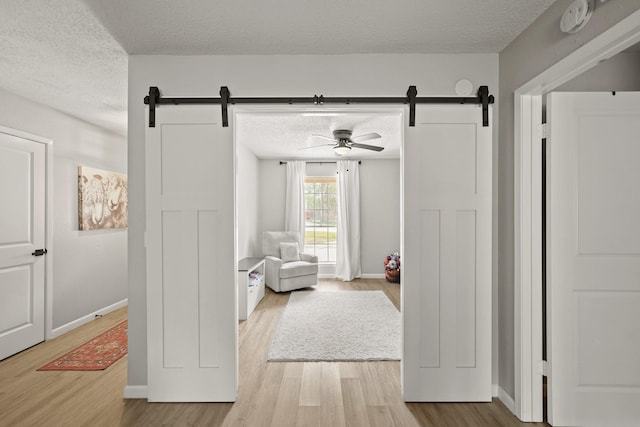 sitting room with a barn door, a textured ceiling, baseboards, and wood finished floors