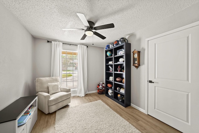 sitting room featuring light wood-style floors, a textured ceiling, baseboards, and a ceiling fan