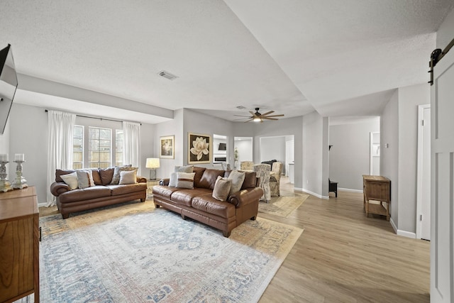 living room featuring a barn door, visible vents, baseboards, ceiling fan, and light wood-style floors