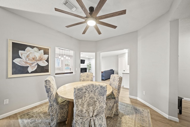 dining space with a fireplace, visible vents, ceiling fan, wood finished floors, and baseboards