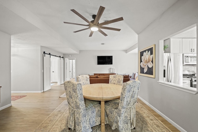 dining space with light wood-style floors, ceiling fan, baseboards, and a barn door