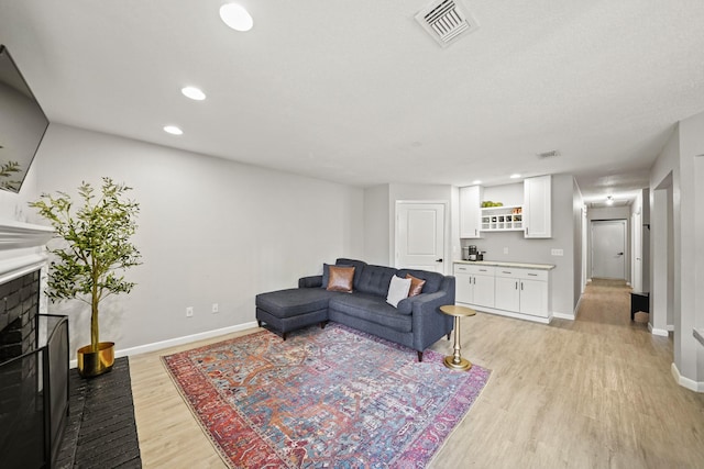 living area featuring a brick fireplace, visible vents, and light wood-style floors