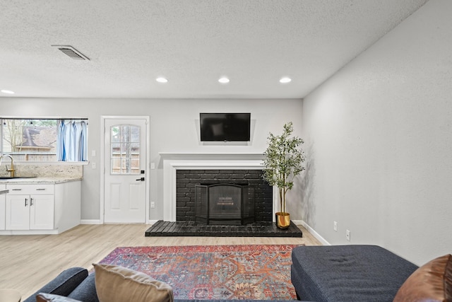 living room featuring light wood-style flooring, visible vents, a fireplace with raised hearth, and a textured ceiling