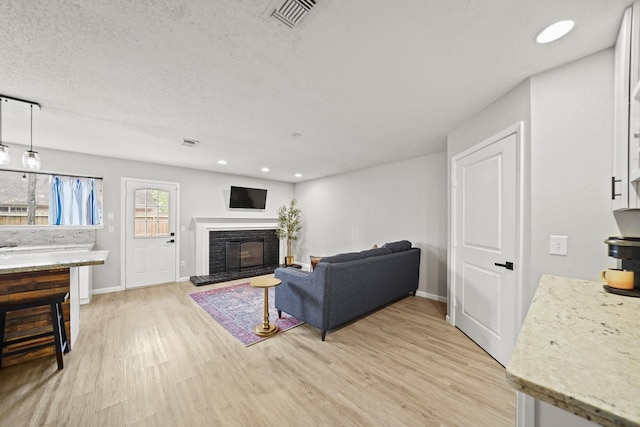 living room with light wood-type flooring, a glass covered fireplace, visible vents, and baseboards